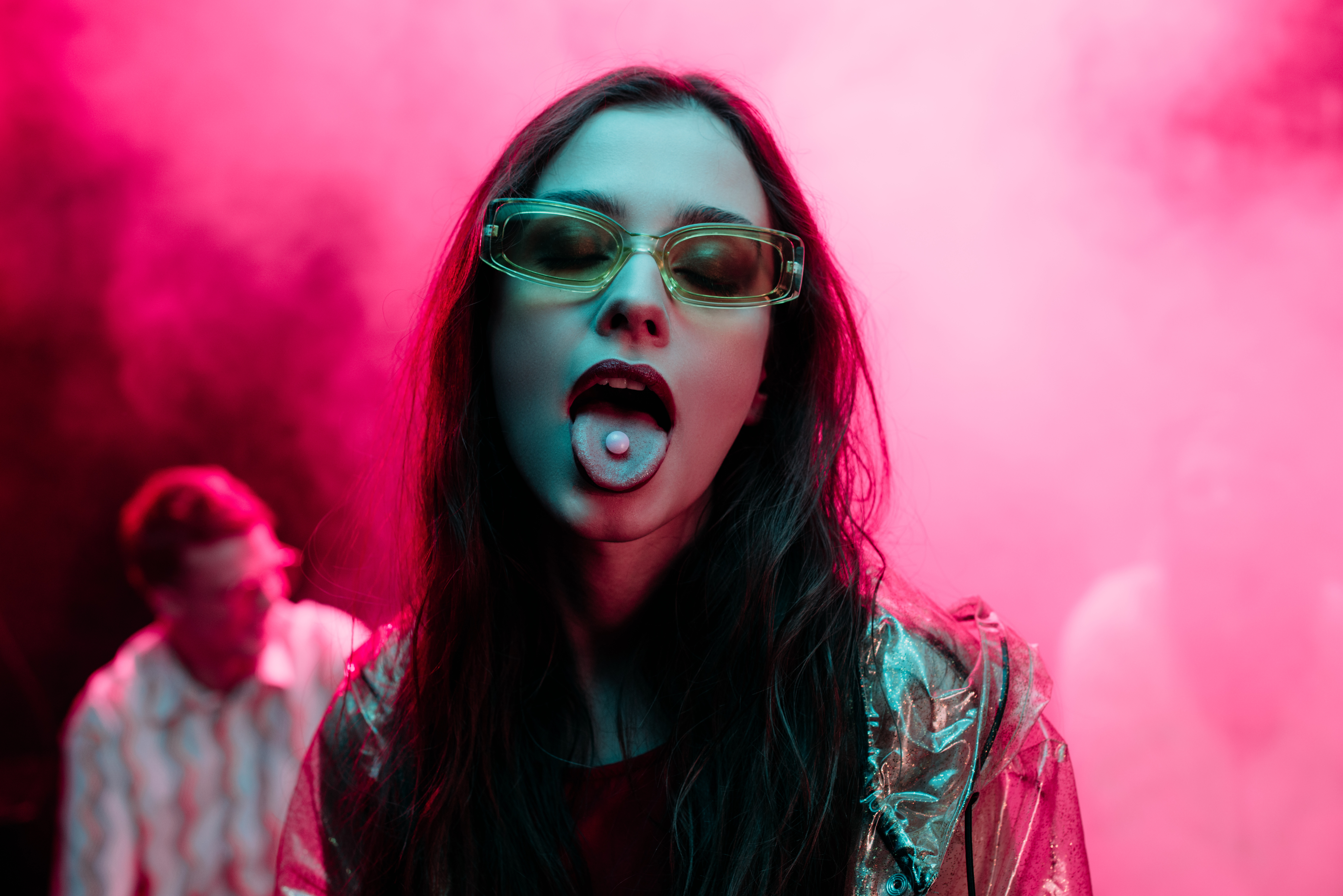 beautiful girl in sunglasses with lsd on tongue in nightclub with pink smoke